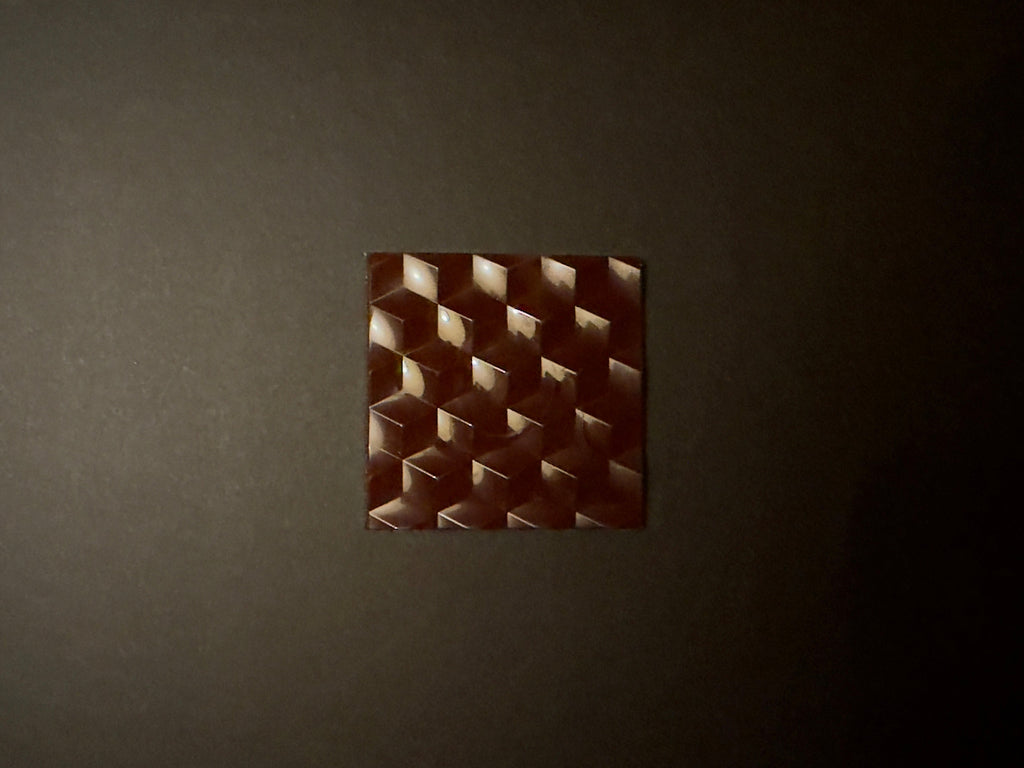 A square shaped chocolate bar with a geometric pattern on a dark background